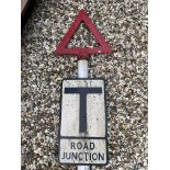 A metal road sign for Road Junction mounted on a tall post, surmounted by a warning triangle.
