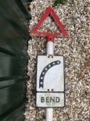 A metal road sign for Bend with integral glass reflective discs, mounted on a tall post,