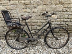 A ladies Raleigh bicycle with Brooks leather saddle and toddler chair to the rear.