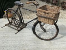 A gents delivery bicycle with basket to the front, on a display stand.
