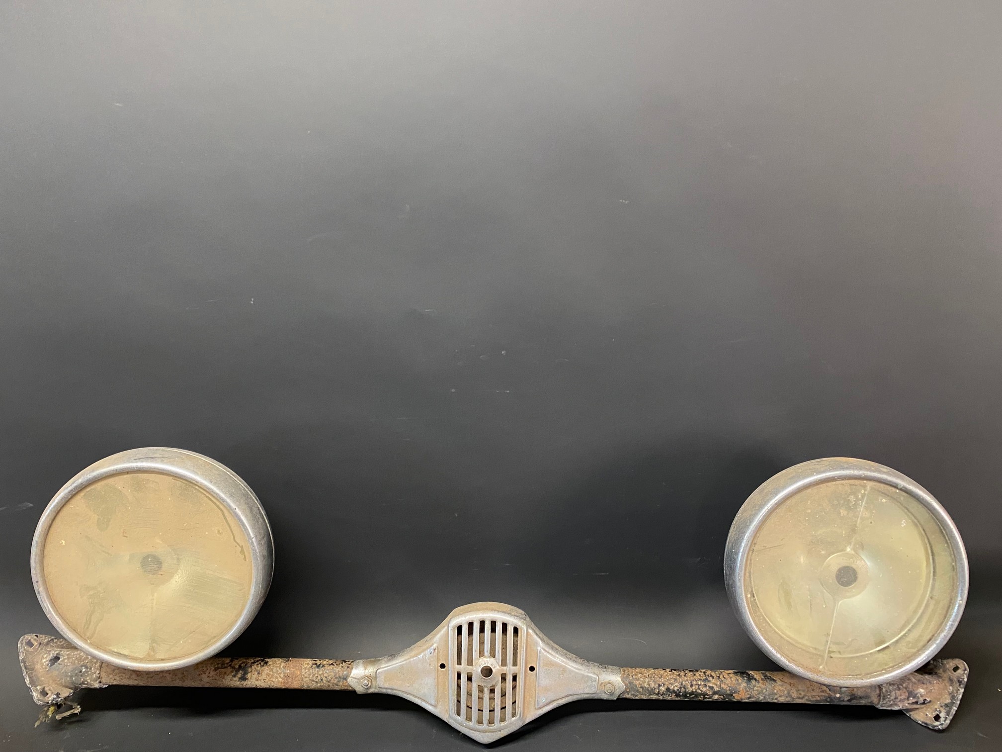 A pair of Lucas L165S headlamps on a bar that has a horn in the centre.