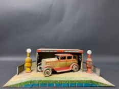 A German tinplate garage with two petrol pumps, illuminated globes and a vintage car, probably