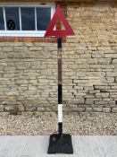 A triangular warning road sign on a metal pole, later base.