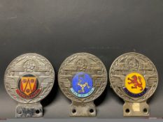 Three St. Christopher car badges, each with a different enamel location inset including the Isle