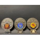 Three St. Christopher car badges, each with a different enamel location inset including the Isle