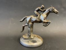 A car accessory mascot in the form of a horse and jockey leaping over a fence, radiator cap mounted.