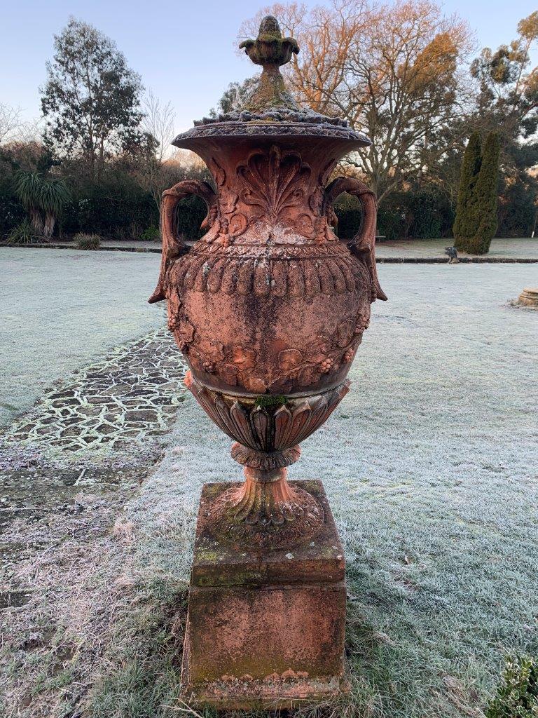 Pair of terracotta two handled lidded urns on plinths