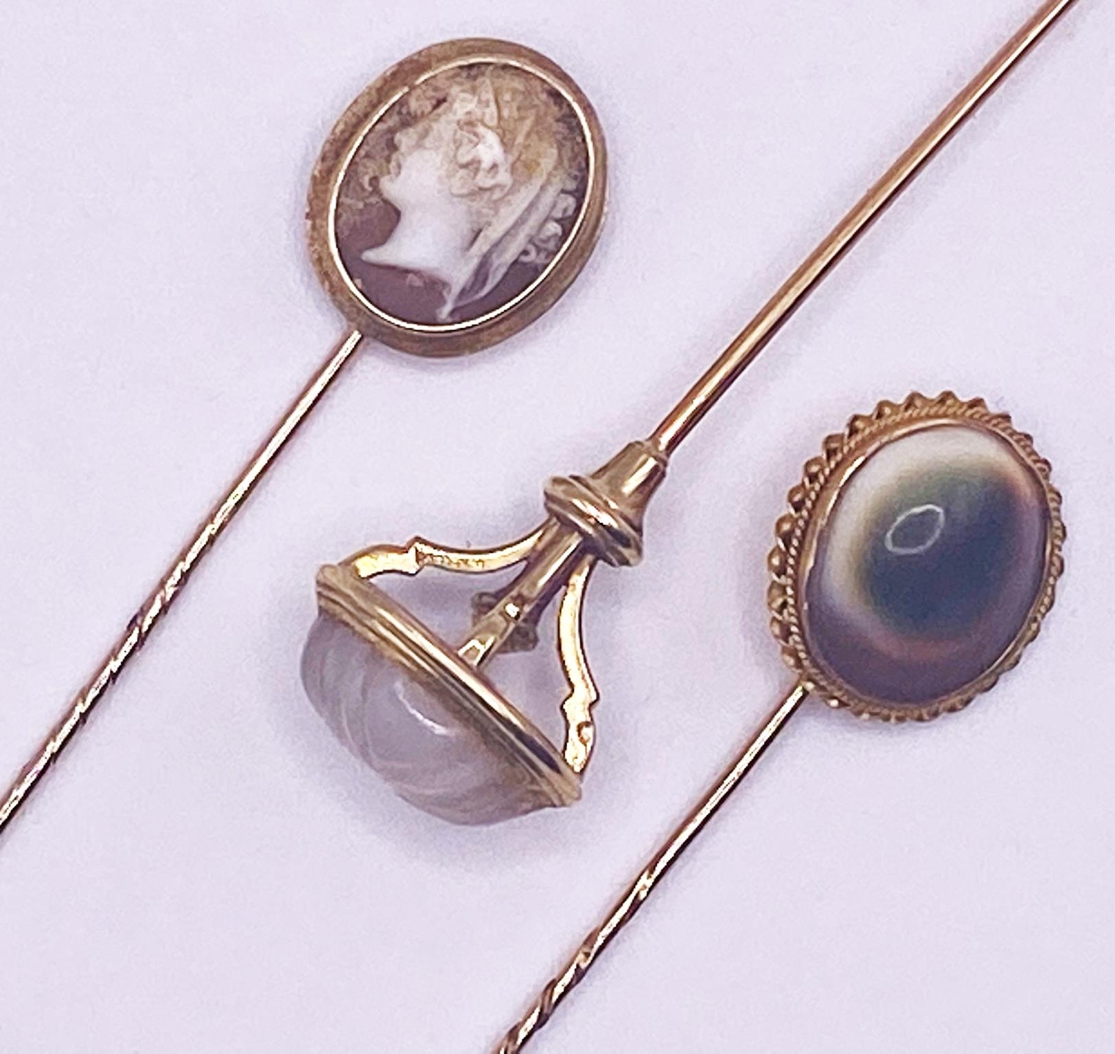 Three yellow metal stick pins set with a cameo of a classical maiden, a carved rock crystal