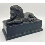 Cast metal probably bronze statue of a recumbent lion upon a stepped square ebonised wooden plinth