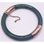 A green jade type stone hinged bangle bracelet with yellow metal mounts. Measuring inner diameter