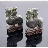 A pair of oriental spinach jade spill vases, in the form of stylized cockerels in two dimensional
