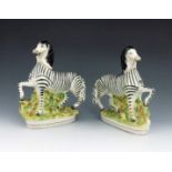 A pair of Staffordshire pottery zebras, circa 1870, modelled with their front leg raised, on a natur