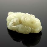 A Chinese pale jade netsuke, in the form of a recumbent shishi and infant, 5.5cm wide