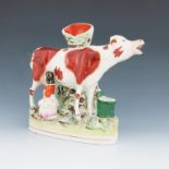A Staffordshire pottery spill vase of a cow and milk maid, circa 1880, the maid modelled seated at t
