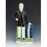 A Staffordshire figure of 'Dan O'Connell', circa 1875, modelled standing beside a draped pedestal, w