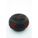 A Chinese red and black lacquer circular covered vessel, carved in high relief with two figures in a