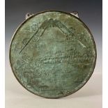 A Japanese bronze roundel wall plaque, cast with a landscape scene with pagodas and boats on a