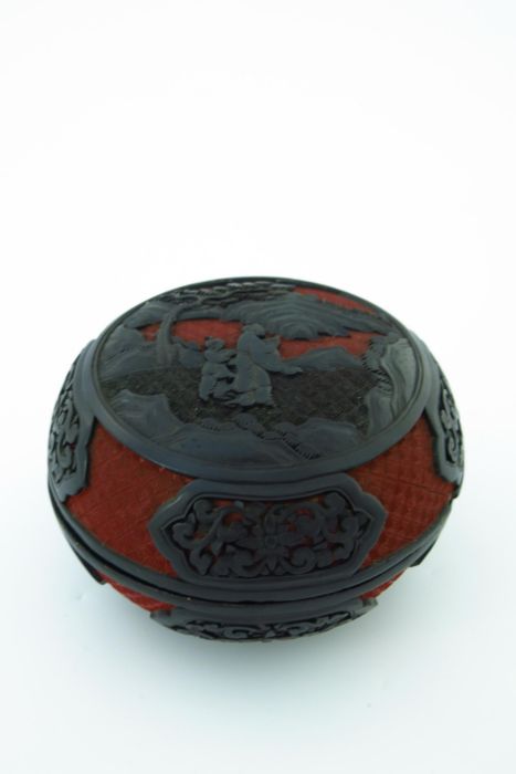A Chinese red and black lacquer circular covered vessel, carved in high relief with two figures in a
