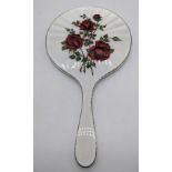 A silver hand mirror, mounted with enamel red roses on a white ground, hallmarked London, 1959,
