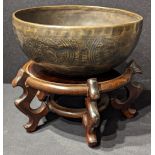 A Tibetan brass singing bowl, raised on a Chinese hardwood stand
