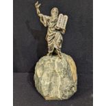 A silver covered sculpture of Moses with the Ten Commandments mounted on a rock, total item height
