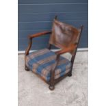 An early 20th century low-seated wooden fireside chair with leather back rest with Coat of Arms or