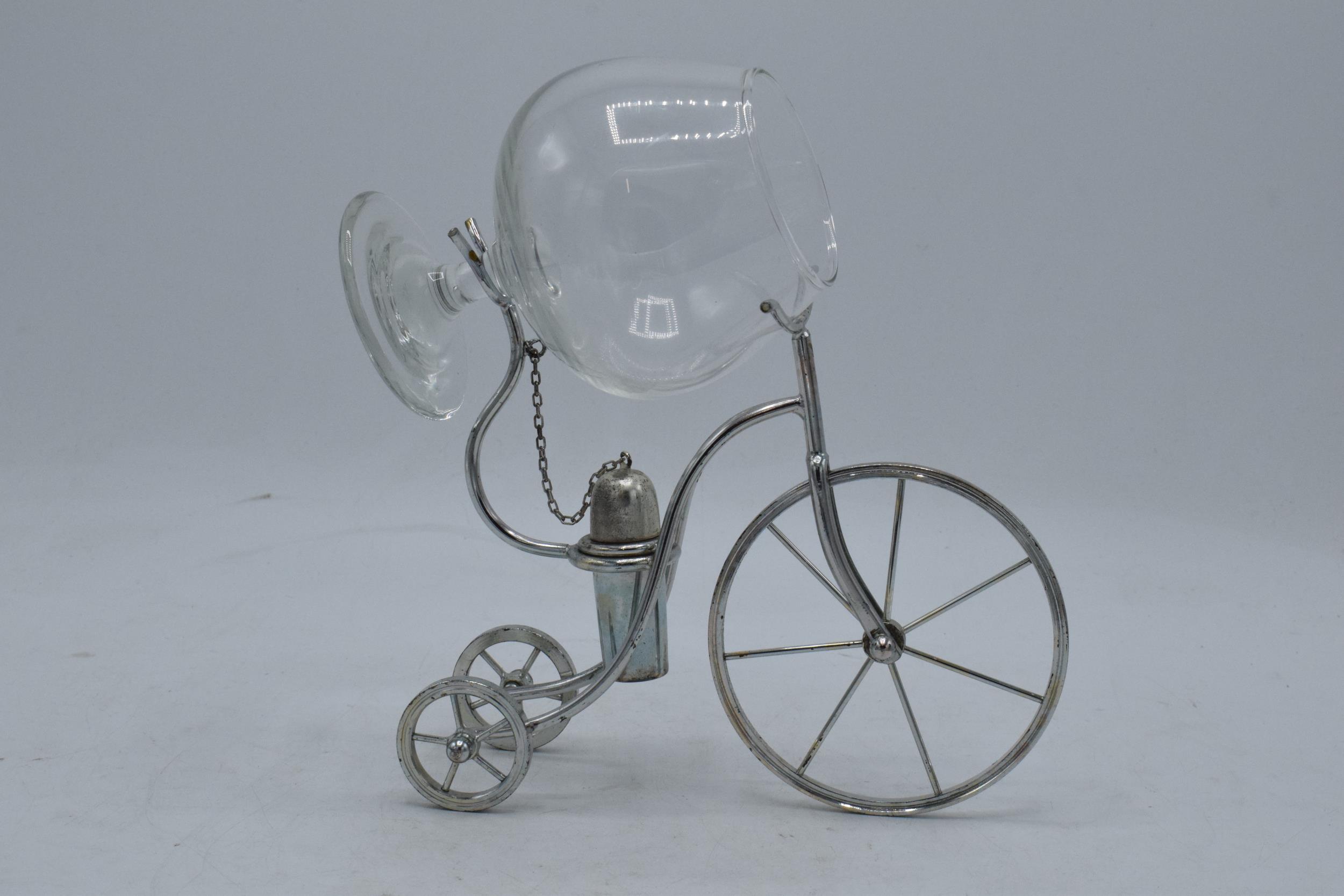 A novelty silver plated brandy warmer in the form of a tricycle / penny farthing style with a glass.