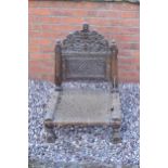 An antique heavily carved wooden low chair with woven seat and twisted iron support, in the Moroccan