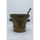 A large antique cast brass mortar and pestle with ornate decoration featuring the devils face.