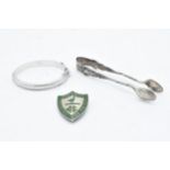 A trio of silver items to include Harrogate College prefect badge, sugar tongs and a child's