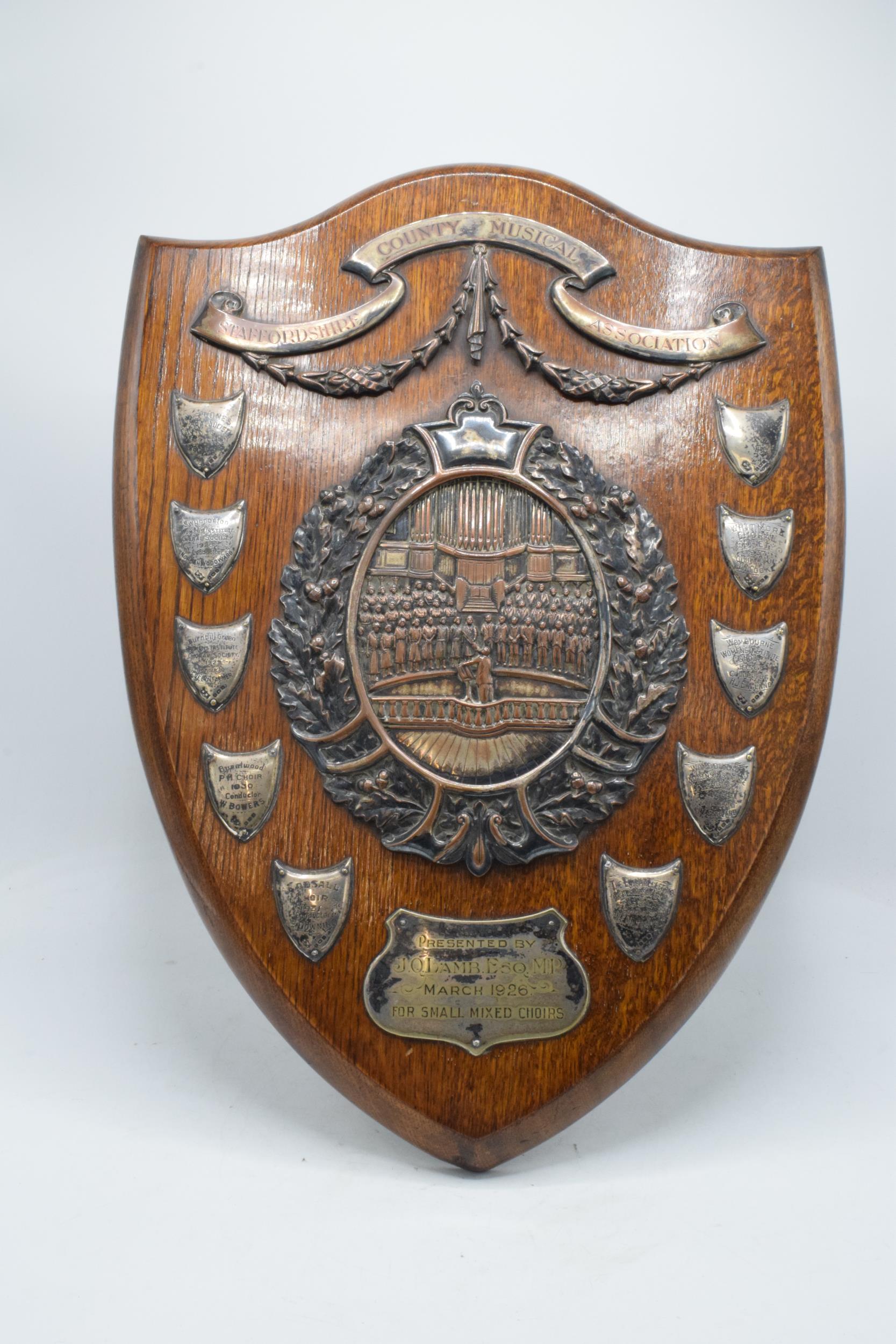 A wooden presentation shield with hallmarked silver name shields and a silver plate central relief