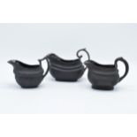 A trio of early to mid 19th century black basalt cream jugs to include 2 examples with detailed