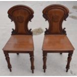 A pair of Victorian oak carved shaped back hall chairs with raised shell motif (2), 86cm tall.