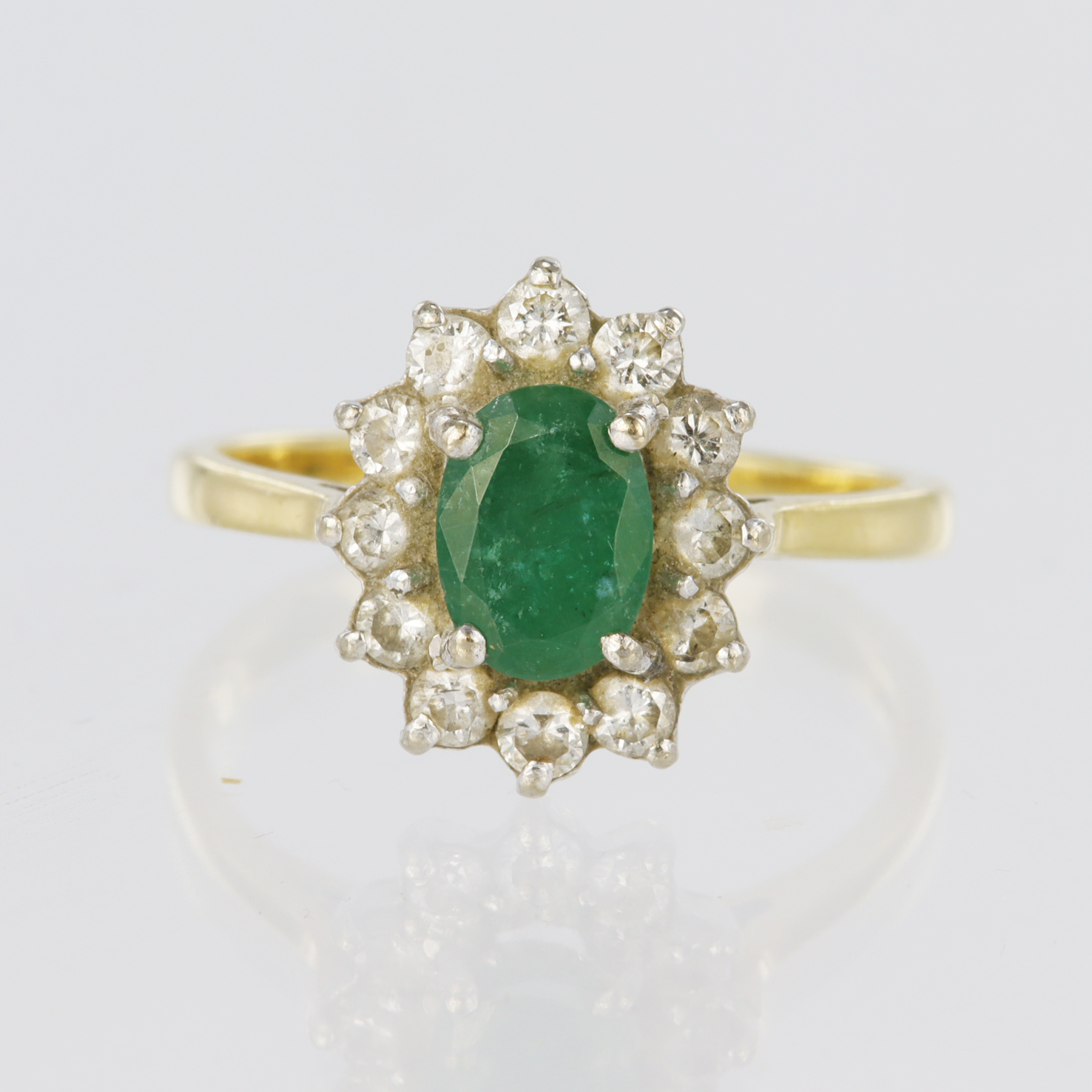 18ct yellow gold ring featuring a central oval emerald measuring approx. 7mm x 5mm, surrounded by