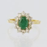 18ct yellow gold ring featuring a central oval emerald measuring approx. 7mm x 5mm, surrounded by