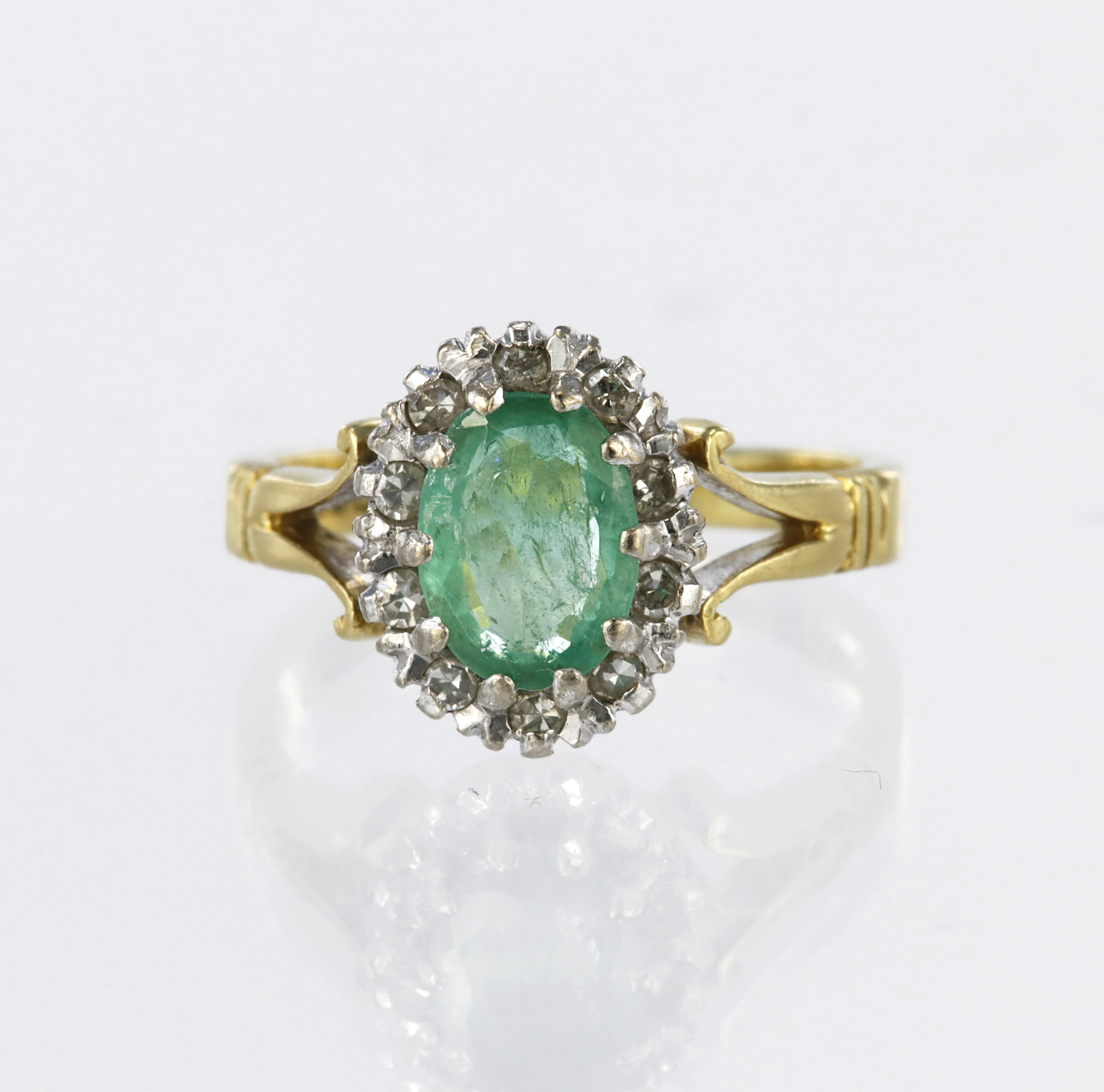 18ct yellow gold cluster ring featuring a central oval emerald measuring approx. 7mm x 5.5mm,