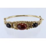 9ct yellow gold hinged bangle, set with graduating cabochon garnets, principle garnet measuring 19mm