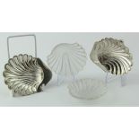 Two silver scallop- shaped butter dishes with glass liners, each one on three ball feet;