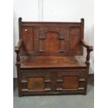 A 17th century style oak monks bench with panelled and carved frame and open arms above a hinged