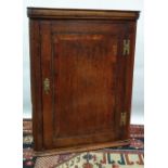 An early 19th century small oak corner cupboard, fitted two shelves with blind crossbanded door