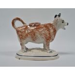 A 19th century English pottery cow creamer with sponged decoration, height 12cm.