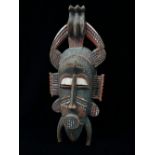 A West African carved wood tribal mask with polychrome decoration, height 51cm.