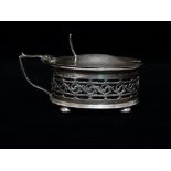 A George V silver hinge lidded mustard pot of oval section with pierced body, raised on four ball