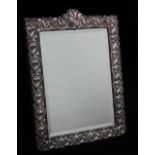 A silver easel dressing table mirror with embossed floral and foliate decoration with vacant