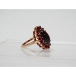 9ct gold and garnet ring - A 9ct gold ring set a large oval cabochon garnet surrounded by sixteen