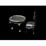 A silver hallmarked doll's house table and chair with Rococo decoration, chair height 5.6cm, table