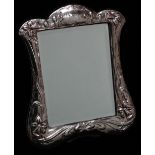 A shaped silver easel dressing table mirror, embossed with daffodils and with a vacant cartouche