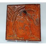 A Relief Glazed Tile - A tile decorated with a seated female and dove under a tree, 25.3 x 24.3cm.