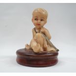 Wax figure of a child - A wax figure of a seated child with a sword on a circular wooden box and