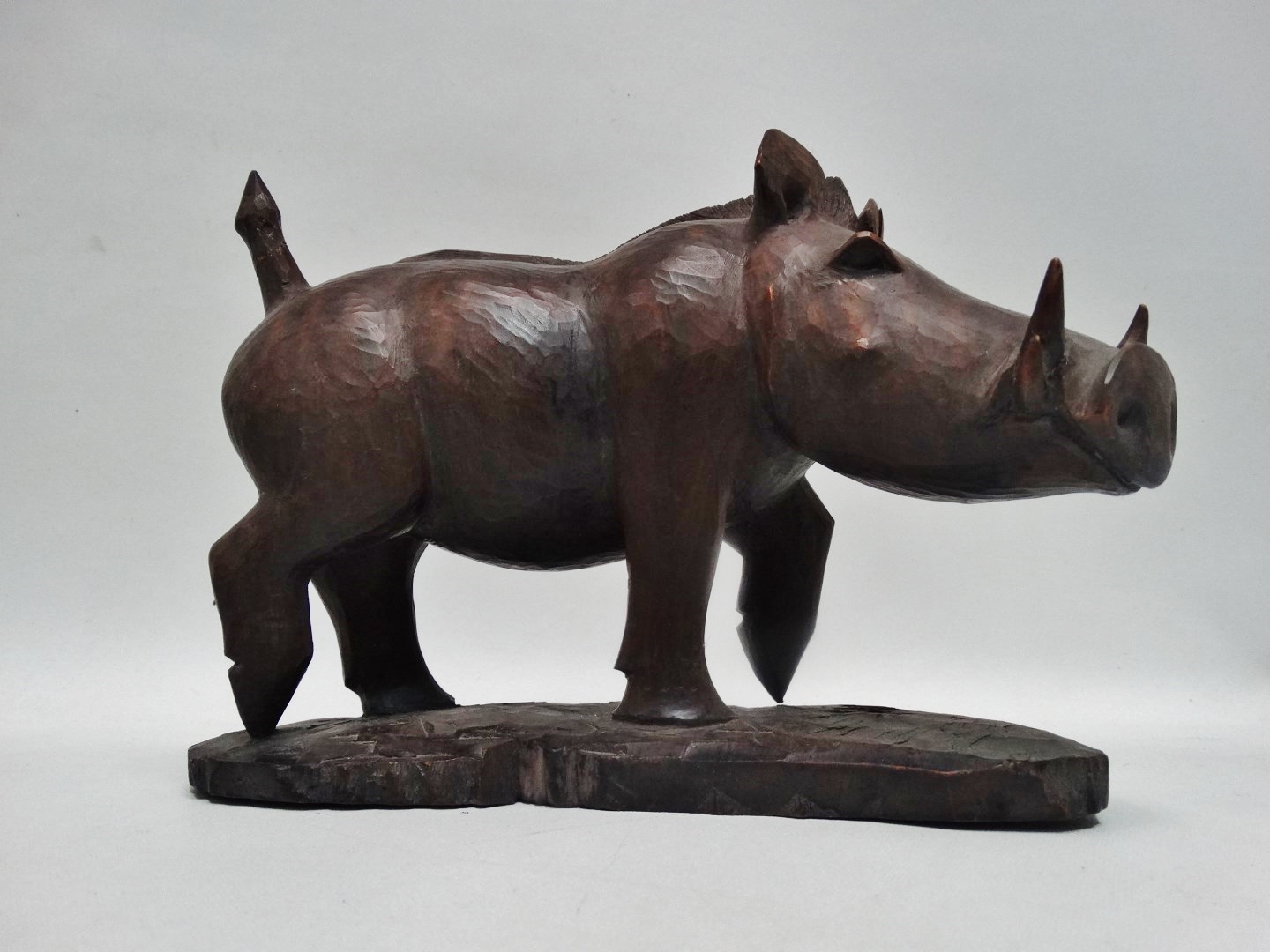 A carved exotic hardwood model of a warthog - standing on a naturalistic base, signed Nganga, height